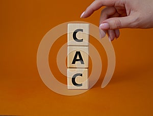 CAC - Customer Acquisition Cost symbol. Wooden cubes with word CAC. Beautiful orange background. Businessman hand. Business and