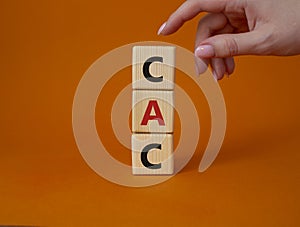 CAC - Customer Acquisition Cost symbol. Wooden cubes with word CAC. Beautiful orange background. Businessman hand. Business and