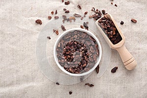 Cacao nibs in white bowl with wooden scoop