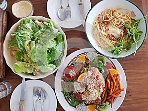 Caesar salad, carbonara and sriracha fried chicken on a wooden t