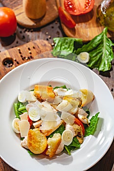 Caesar salad with chicken breast, eggs, croutons, parmesan cheese on white plate. Top view