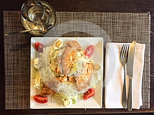 Caesar salad with chicken. cutlery on a white cloth napkin. square plate