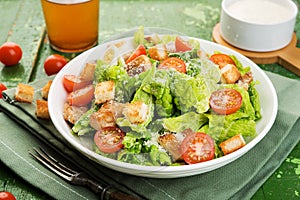 Caesar salad with chicken fillet, tomatoes, croutons and parmesan in a plate on a rustic wooden background