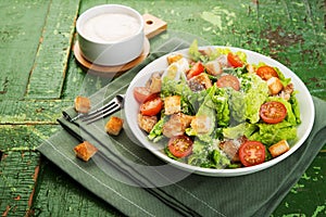 Caesar salad with chicken fillet, tomatoes, croutons and parmesan in a plate on a rustic wooden background