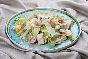 Caesar salad with chicken, Parmesan and cherry tomatoes. In a blue plate on a textile background