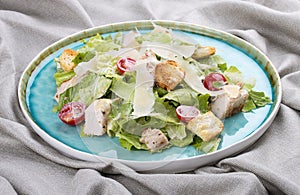 Caesar salad with chicken, Parmesan and cherry tomatoes. In a blue plate on a textile background