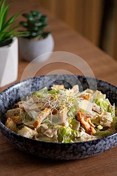 Caesar salad with chicken strips, croutons, Parmesan, lettuce, drizzled with dressing, served in bowl on wooden table.