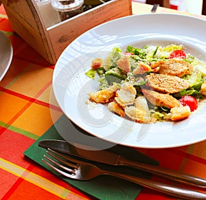 Caesar salad with croutons,eggs, cherry tomatoes and grilled chicken in a white plate on a table in a restaurant