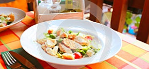Caesar salad with croutons,eggs, cherry tomatoes and grilled chicken in a white plate on a table in a restaurant