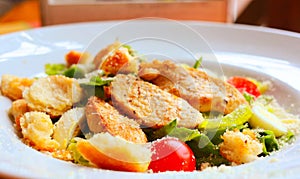 Caesar salad with croutons,eggs, cherry tomatoes and grilled chicken in a white plate on a table in a restaurant