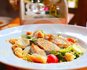 Caesar salad with croutons,eggs, cherry tomatoes and grilled chicken in a white plate on a table in a restaurant