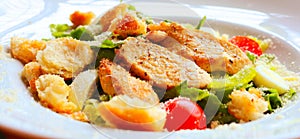 Caesar salad with croutons,eggs, cherry tomatoes and grilled chicken in a white plate on a table in a restaurant