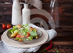 Caesar salad with croutons, quail eggs, cherry tomatoes and grilled chicken in white plate on dark rustic table
