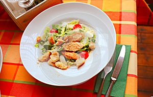 Caesar salad with croutons, quail eggs, cherry tomatoes and grilled chicken in a white plate on a table in a restaurant