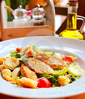 Caesar salad with croutons, quail eggs, cherry tomatoes and grilled chicken in a white plate on a table in a restaurant