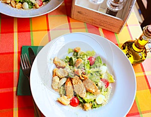 Caesar salad with croutons, quail eggs, cherry tomatoes and grilled chicken in a white plate on a table in a restaurant