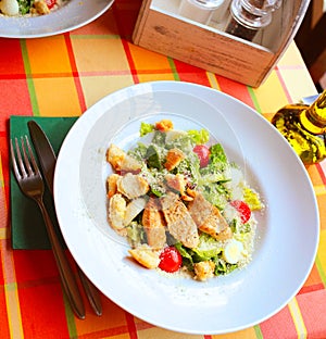 Caesar salad with croutons, quail eggs, cherry tomatoes and grilled chicken in a white plate on a table in a restaurant