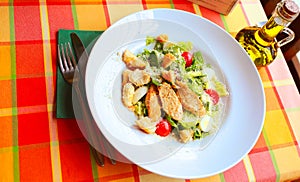 Caesar salad with croutons, quail eggs, cherry tomatoes and grilled chicken in a white plate on a table in a restaurant