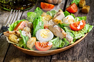 Caesar salad with croutons, quail eggs, cherry tomatoes and grilled chicken in wooden plate