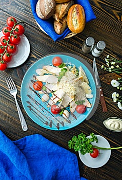 Caesar salad with croutons, quail eggs, cherry tomatoes and grilled chicken in wooden plate on dark rustic table