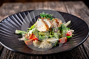 Caesar salad with fresh vegetables and crispy chicken on wooden background
