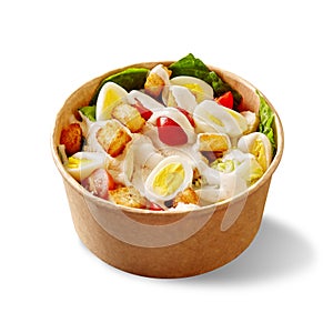 Caesar salad with lettuce, cherry tomatoes, quail eggs, croutons, chicken and sauce in cardboard bowl on white