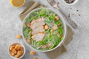 Caesar salad with lettuce, grilled chicken breast, parmesan cheese and croutons in a bowl on a gray concrete background.