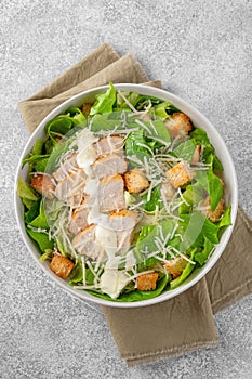 Caesar salad with lettuce, grilled chicken breast, parmesan cheese and croutons in a bowl on a gray concrete background.