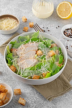 Caesar salad with lettuce, grilled chicken breast, parmesan cheese and croutons in a bowl on a gray concrete background