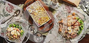 Caesar salad, Olivier salad and salad herring under fur coat in plate on wooden rustic background with vintage book. Holiday food