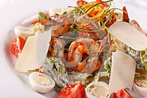 Caesar salad with quail eggs, cherry tomatoes, Parmesan cheese and grilled shrimps in white plate on light table.