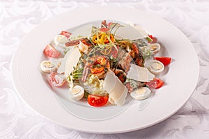 Caesar salad with quail eggs, cherry tomatoes, Parmesan cheese and grilled shrimps in white plate on light table.