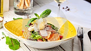Caesar salad with salmon. mix of salads, cherry tomatoes, parmesan cheese, basil. A dish in a ceramic plate is on wooden table