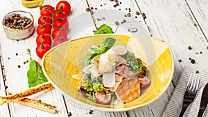 Caesar salad with salmon. mix of salads, cherry tomatoes, parmesan cheese, basil. A dish in a ceramic plate is on a wooden table