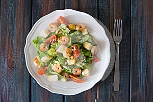 Caesar salad with shrimps in a white plate top view