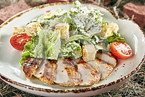 Caesar Salad with Sliced Chicken Fillet on Rustic Hay Background