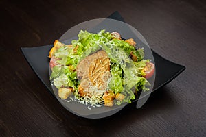 Caesar salad with tongue on a black plate on brown wooden table