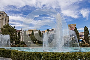 Caesars Palace Hotel, Casino and resort along the Las Vegas strip with tall lush green trees, water fountains, statues, blue sky