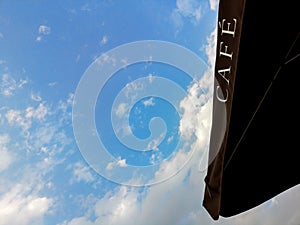 CAFE - cafe sign on a black umbrella against the blue sky and clouds