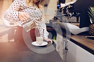 Cafe employee barista pouring hot foamed milk to glass