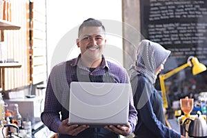 Cafe owner at his coffee shop counter using laptop. his partner working in a background