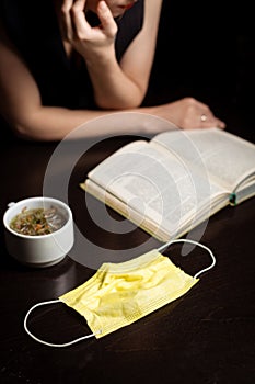 Cafe and pandemic. Medical mask, cup and open book. Dark background. End of quarantine