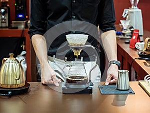 Cafe professional barista brews coffee by an alternative method in pour over, filter on a dark background. Coffee maker and drip k