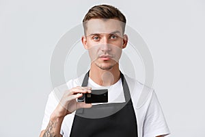 Cafe and restaurants, coffee shop owners and retail concept. Serious-looking handsome salesman, waiter in black apron