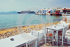 Cafe table and cruise liner in Aegean sea. Chora, Mykonos island, Greece