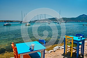 Cafe tableon beach in Adamantas town on Milos island with Aegean sea with boats in background