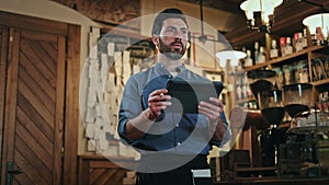 Cafe worker holding handheld order-taking device and tending customers indoors