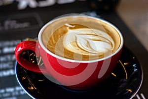 Caffee latte macchiato cappuccino in red mug in cafe house with milk foam art photo