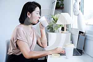 caffeine addiction concept with Asian woman drinking too much coffee while working on computer photo