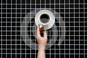 Caffeine and sleep problems. Drinking coffee before bed. A cup of black coffee on black checkered background